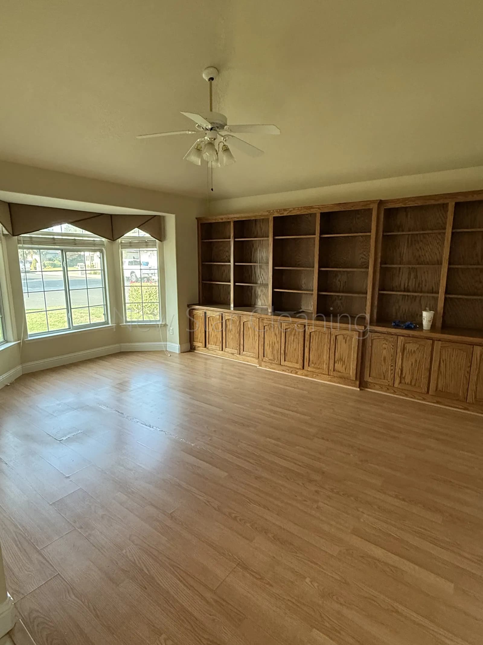 Empty den with wiped full-wall oak built-in bookcases and bay window after a New Star move-out cleaning