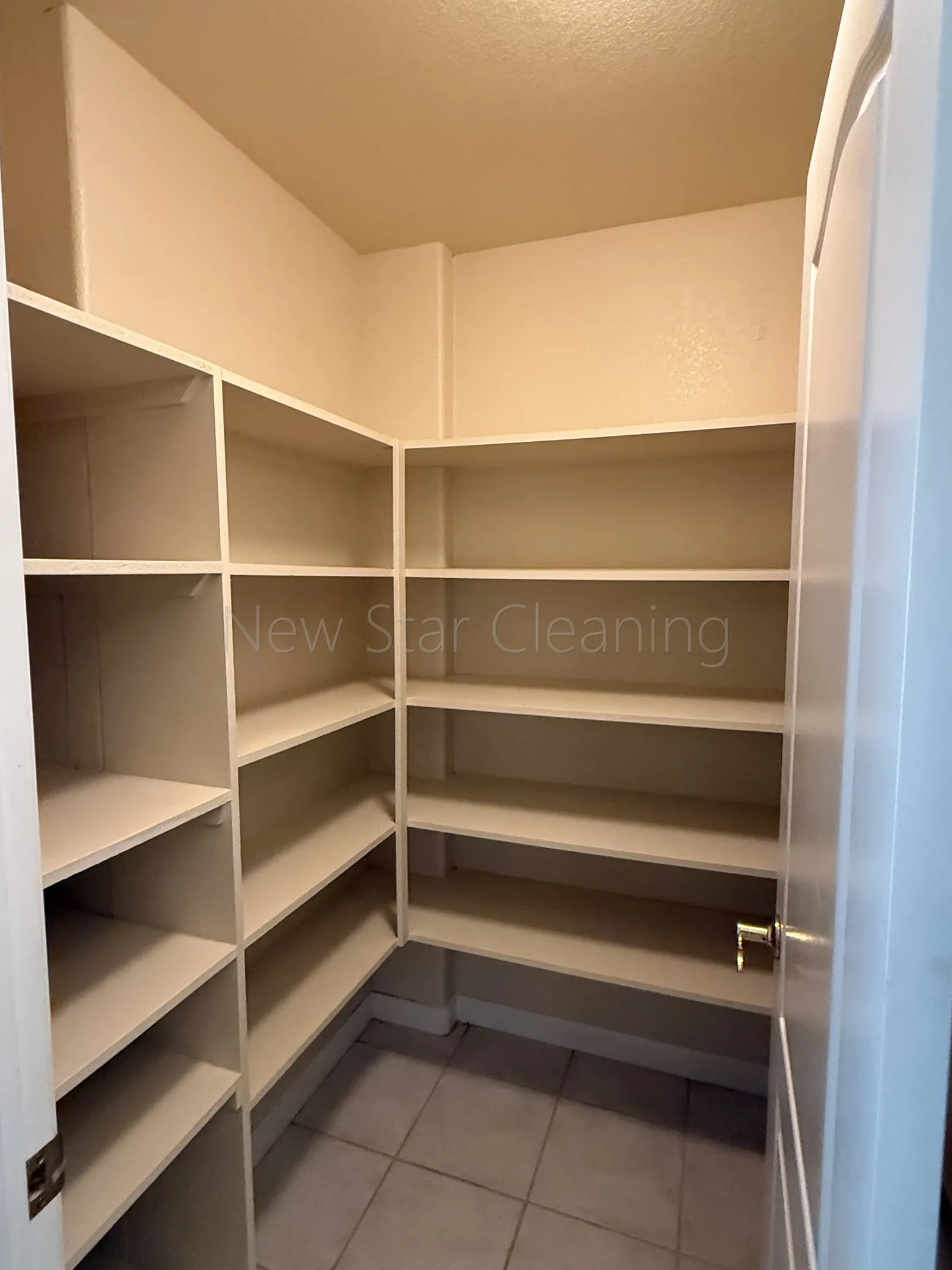 Empty walk-in corner pantry with wiped shelves and clean tile floor after a New Star move-out cleaning