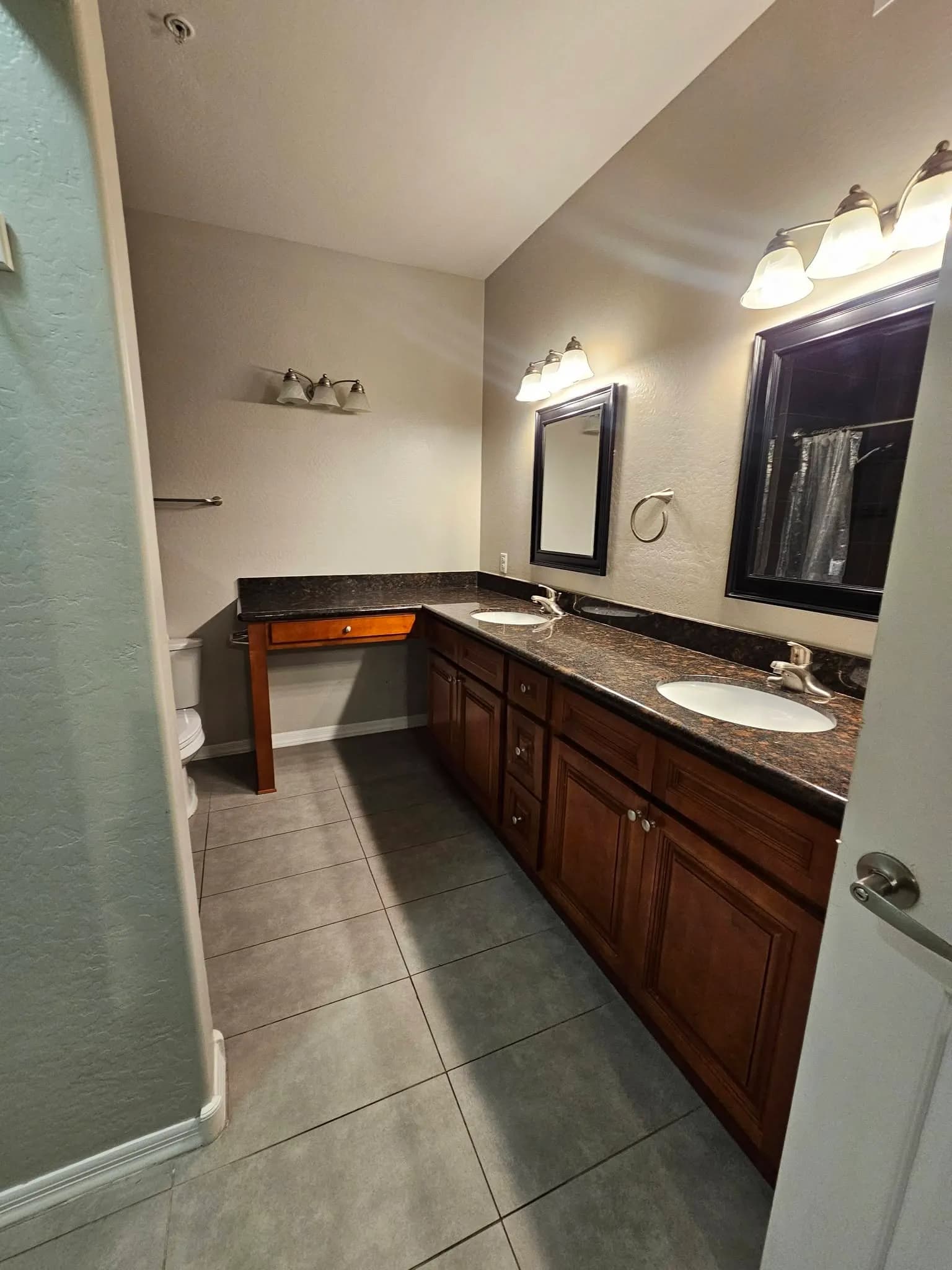 Double bathroom vanity with dark wood cabinets, mirrors, and a light tile floor